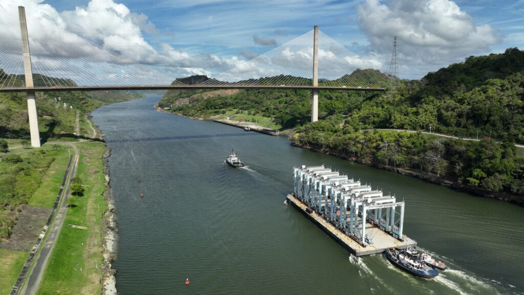 Foss Maritime vessel transporting cargo under a large bridge over a river with lush green hills.